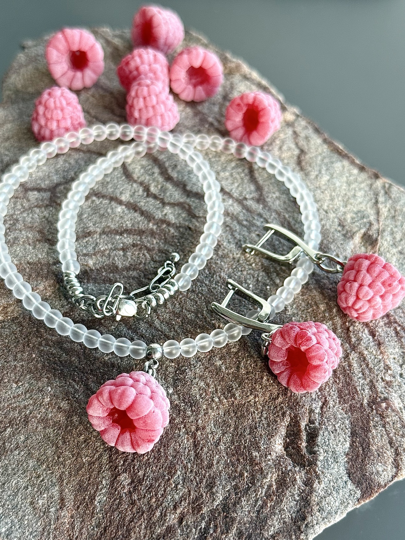 Hand-shaped raspberry jewellery arranged on textured stone