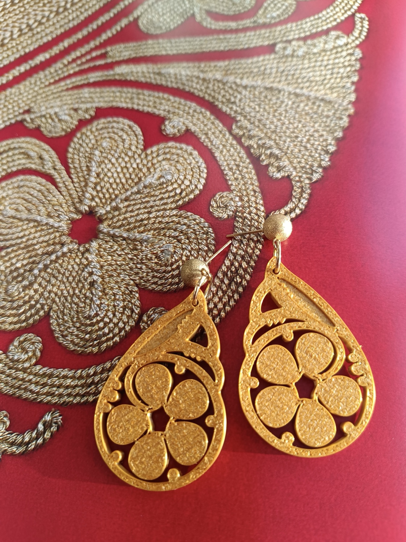 Gold earrings inspired by traditional embroidery on red textile